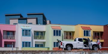 Colorful townhouses with a white pickup truck and people nearby.