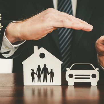 Hands protecting paper cutouts of a family, house, and car symbolizing insurance.