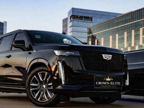 Black Cadillac SUV parked in front of modern glass buildings at sunset.