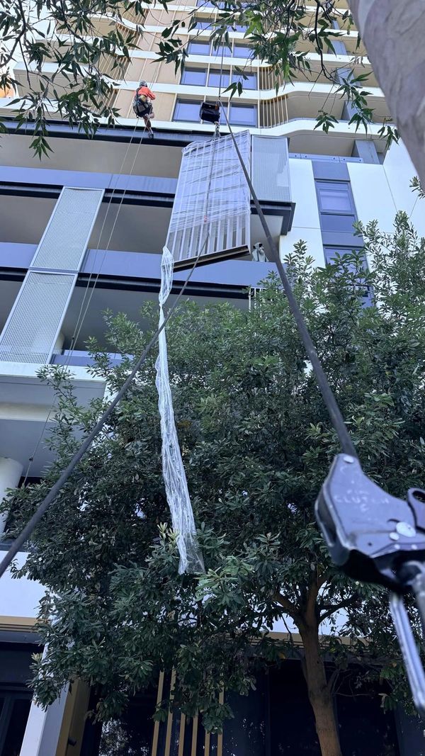 A worker rappelling down a building to install or repair a window screen.