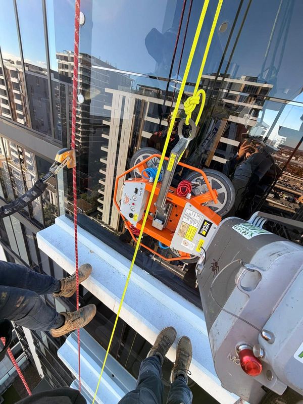 Workers suspended outside a high-rise building using ropes and machinery for maintenance.