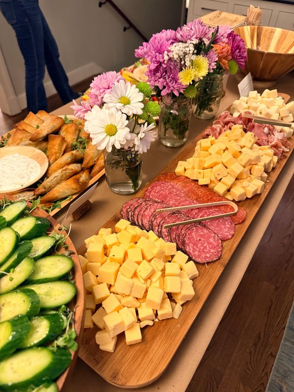 Charcuterie board with cheese, salami, fresh flowers, and appetizers on a table.
