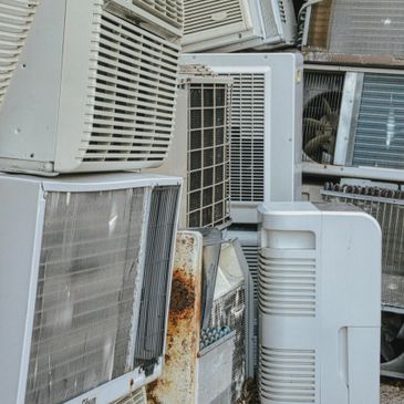 A stack of various air conditioning units piled together outdoors.