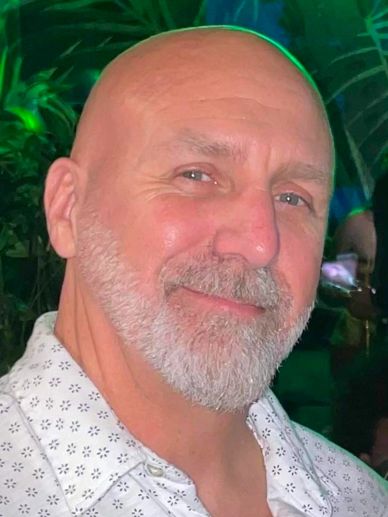 Smiling bald man with a white beard in a patterned shirt.