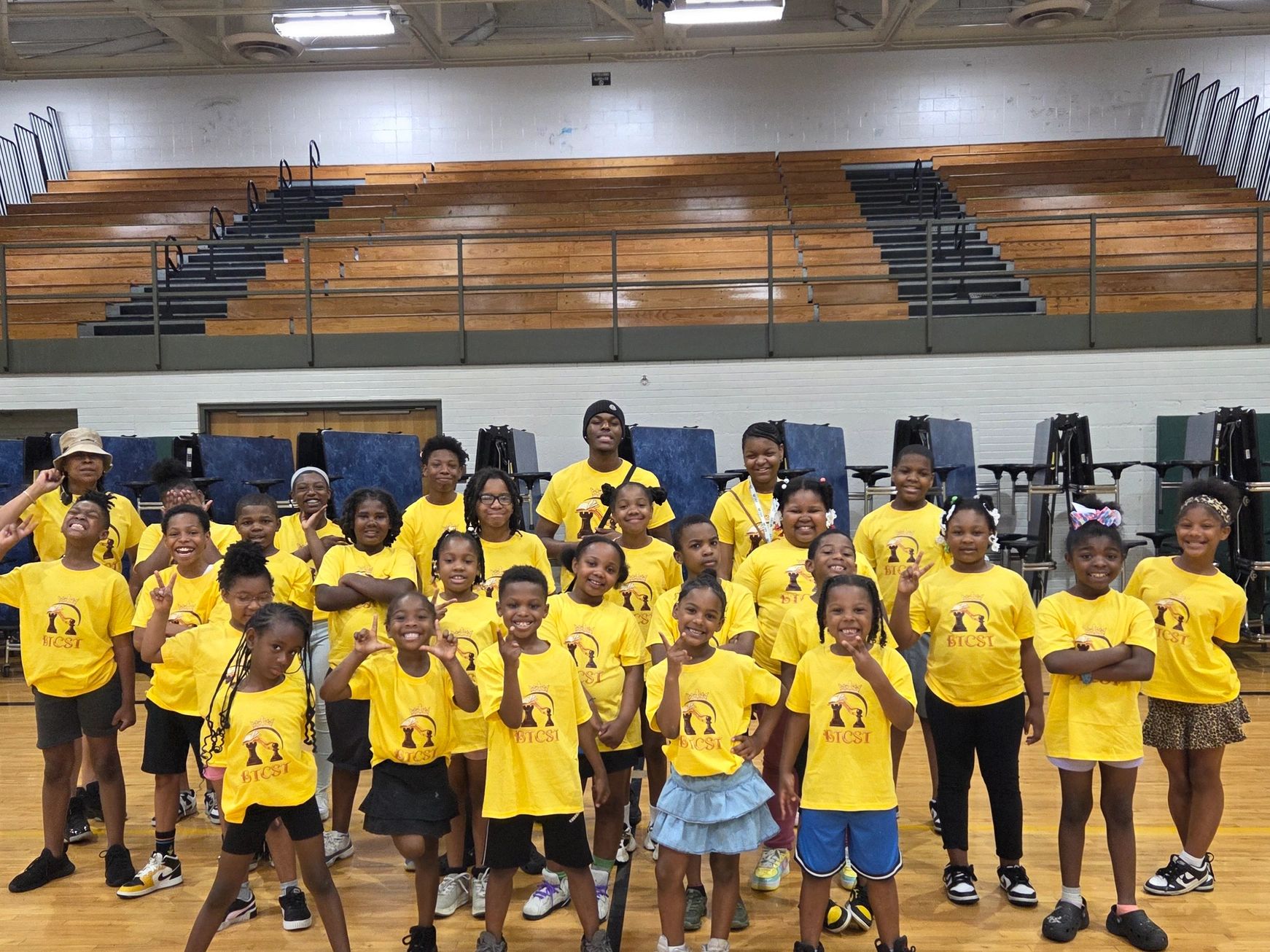 Kids and adults in yellow shirts posing indoors on basketball court.