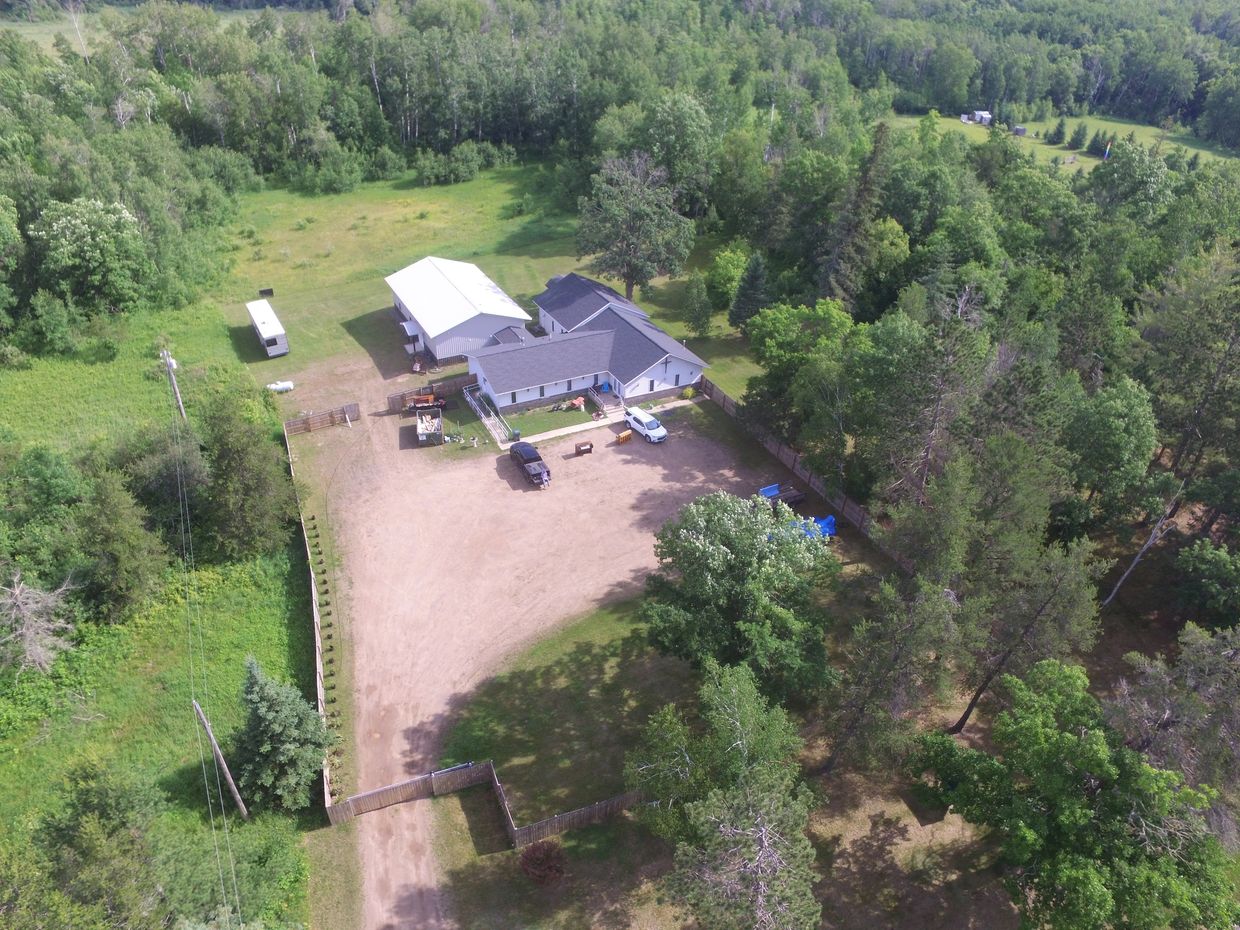 A rural house with vehicles and trees around.