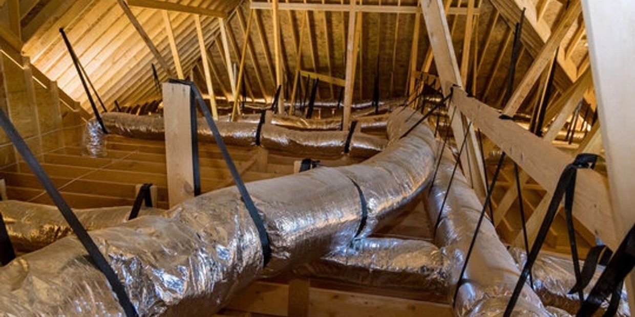 Insulated HVAC ducts installed in a wooden attic framework.