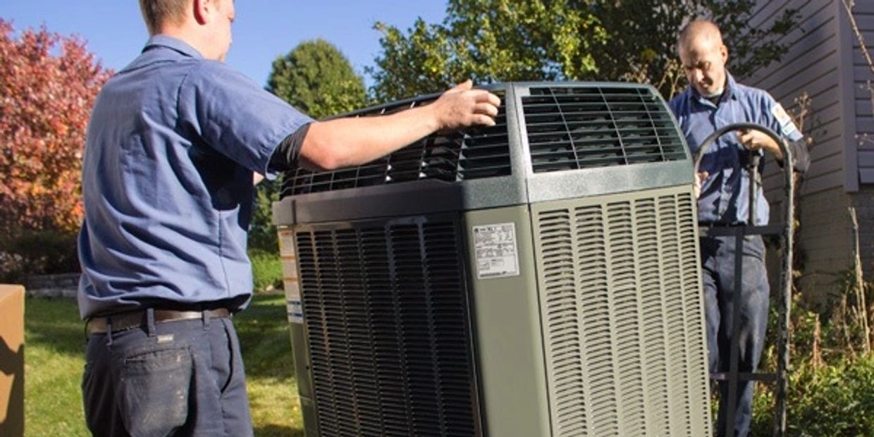 Two technicians installing a large air conditioning unit outside a house.