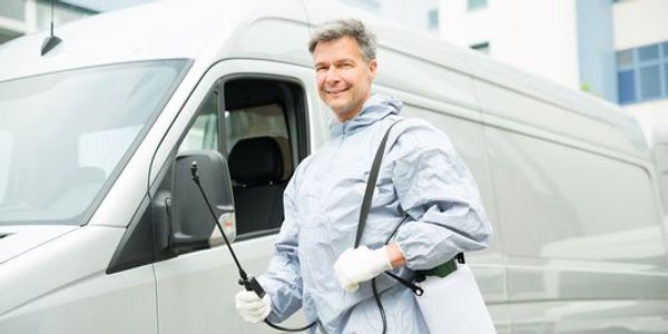 Exterminator man with pest control gear standing in front of his work van