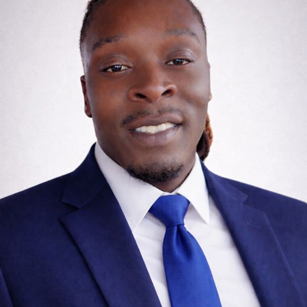 Confident man in a navy suit with a blue tie smiling.