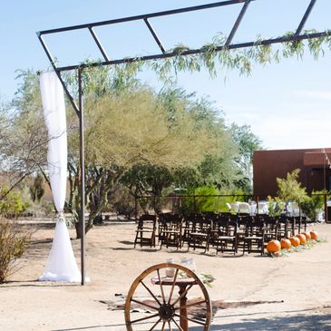 Outdoor rustic wedding setup with wooden chairs and pumpkins.