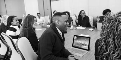 A conference room full of people at a meeting table looking onto the right. 