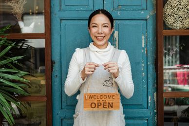 A woman holding a sign that says welcome we are open. 