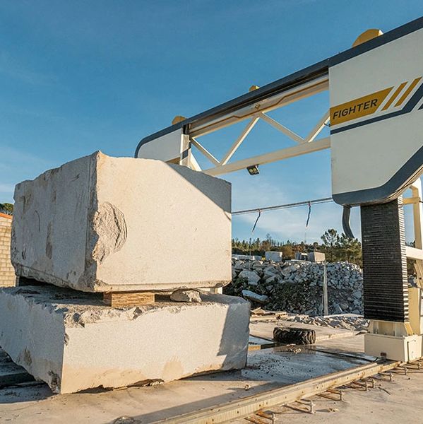 Large stone blocks stacked at a cutting machine site under a clear sky.