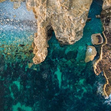 Aerial view of rocky coastline with clear blue water.