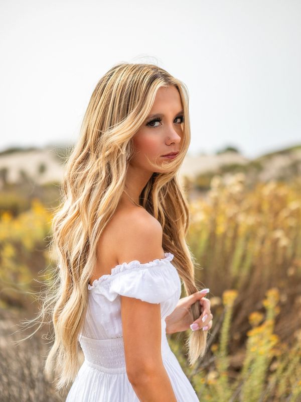 Young woman in white dress standing in a field with long blonde hair.