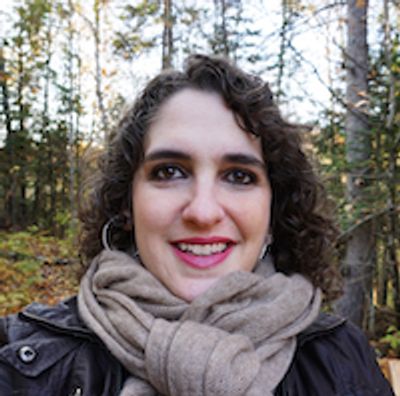 Autumn forest backdrop; white woman w/ brown curly hair, red/pink lipstick, hoop earrings, tan scarf