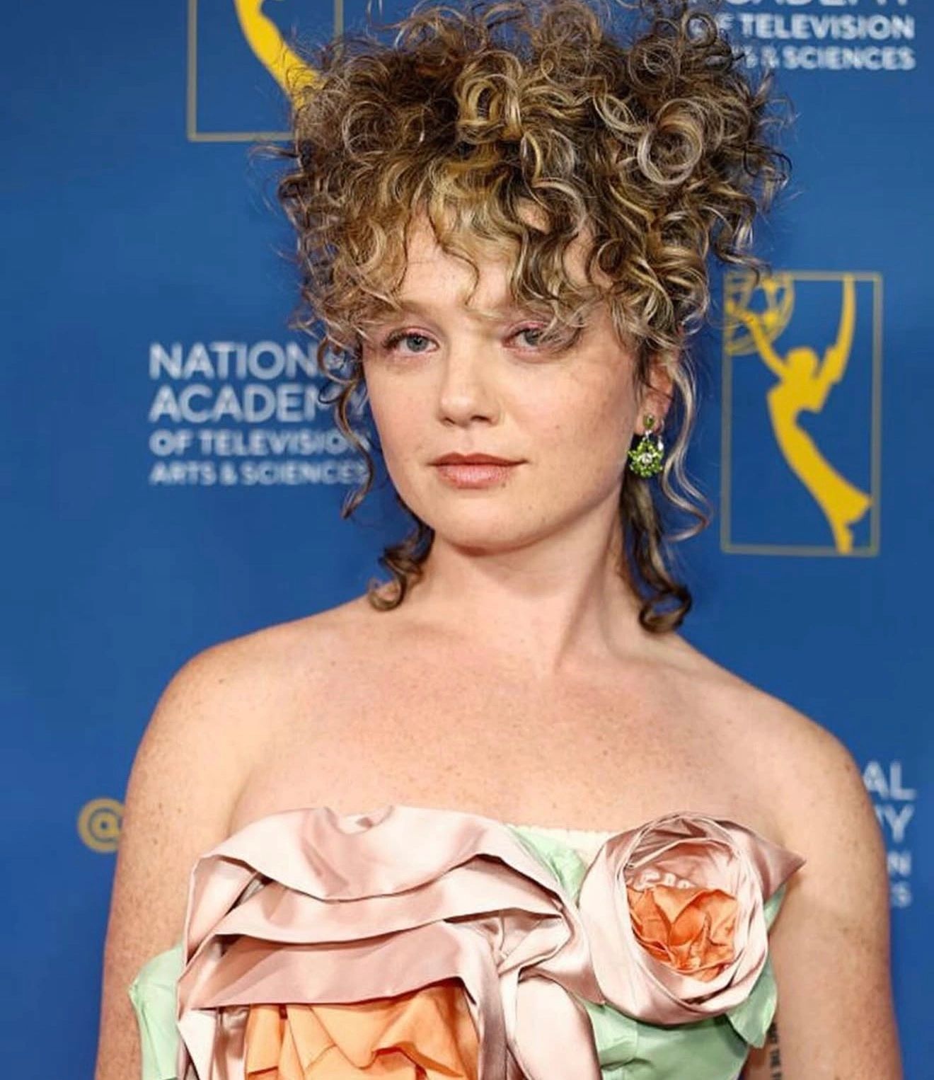 Person with curly hair posing in front of a National Academy backdrop.