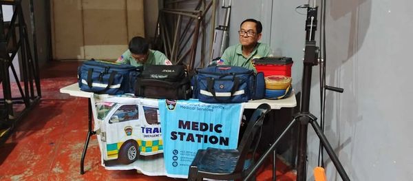 Two medical personnel sit at a medic station table with emergency bags.