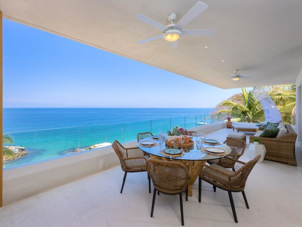 Oceanfront balcony dining area with wicker chairs and glass table.