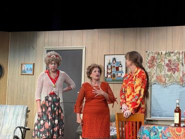 Three women engaged in a dramatic scene inside a vintage living room.
