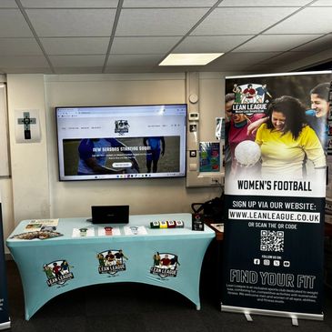 Lean League women's football promotional booth with banner and table setup.