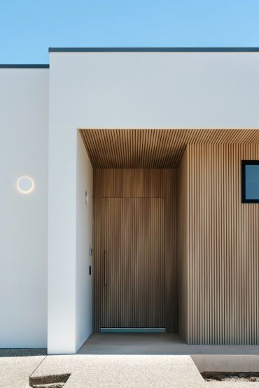Modern entrance with vertical wooden slats and a minimalist light on white wall.