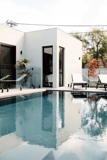 Modern white house with a serene pool and lounge chairs.