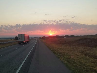 Sunset on a highway with a truck driving away.