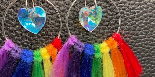 circular silver earrings with a crystal heart in the middle, rainbow-colored strands are attached al