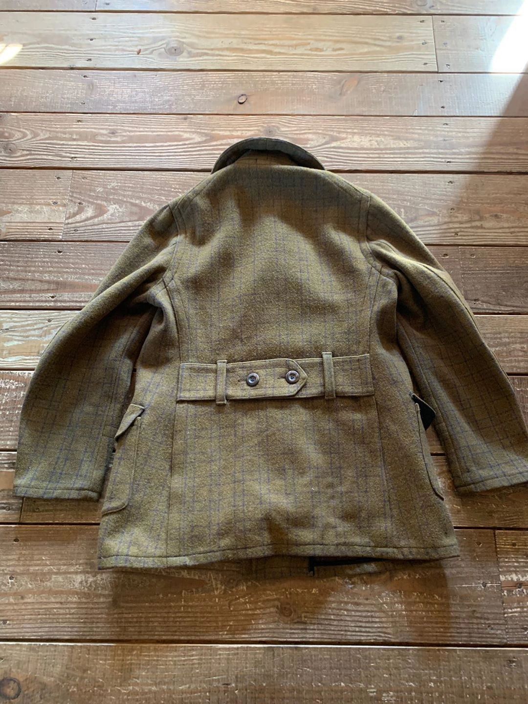 Vintage brown wool coat laid flat on wooden floor.