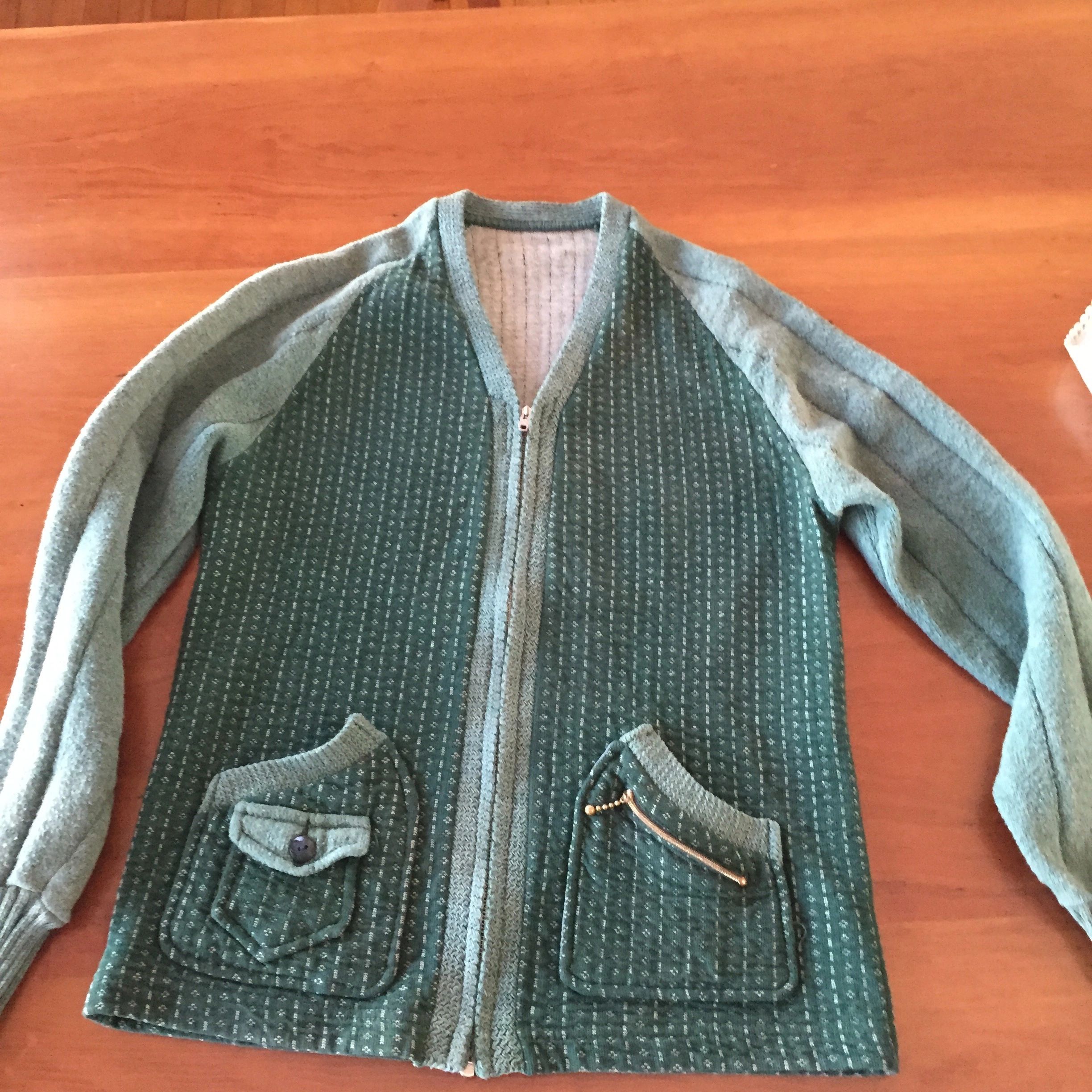 Green zip-up sweater with textured pattern and pockets on a wooden surface.