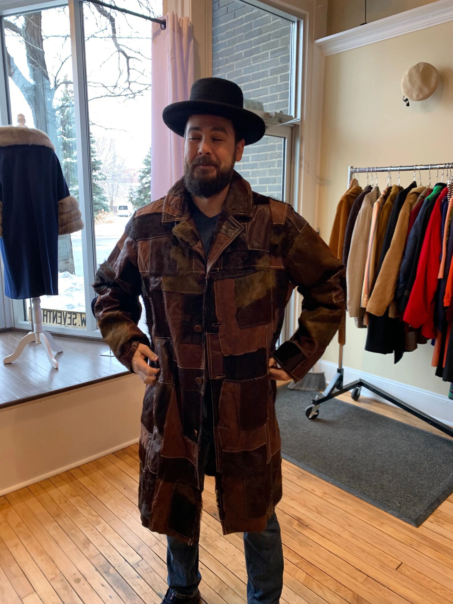 Man in a patchwork leather coat and black hat inside a clothing store.