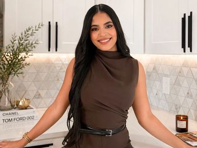 Woman with long black hair smiling in a kitchen.