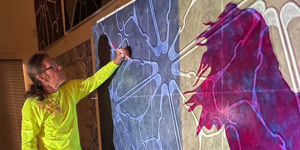 Man in yellow shirt painting intricate patterns on a large canvas.