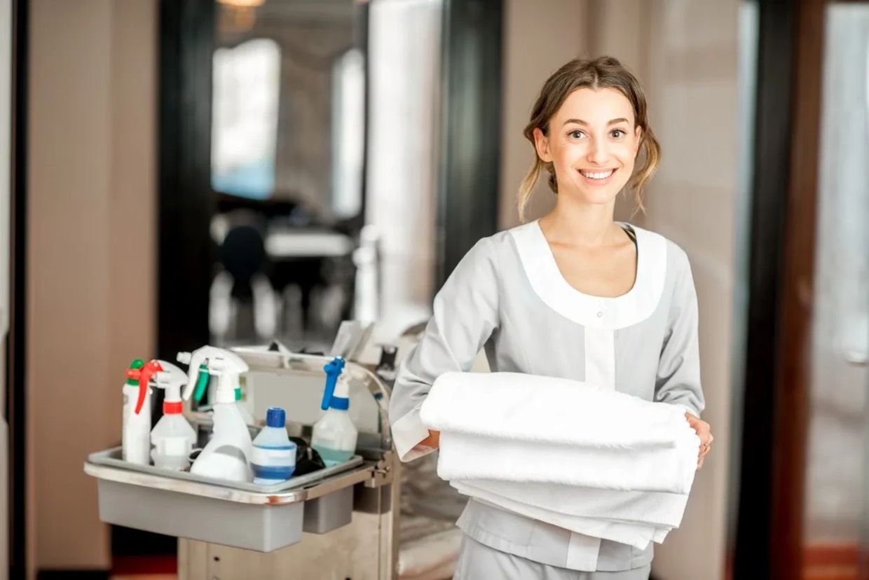 Housekeeper next to the housekeeping cart with clean bed sheets in hand