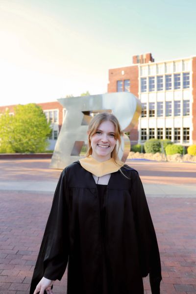 Graduate smiling in cap and gown outdoors.