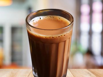 A glass of hot tea with a creamy froth on top.