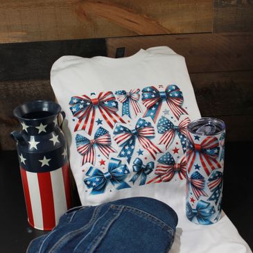 Patriotic-themed apparel and accessories featuring stars, stripes, and bows in red, white, and blue.