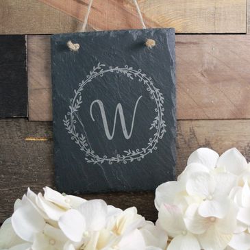Slate sign with 'W' and white flowers on wooden background.