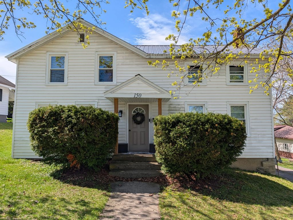 White two-story house with bushes and a small porch under a blue sky.