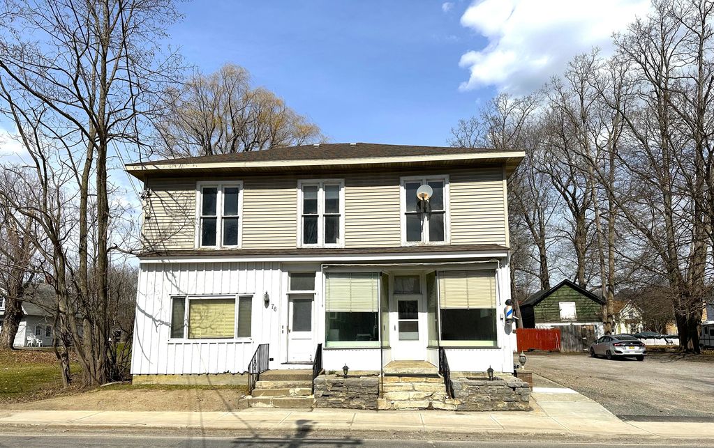 Old two-story house with beige siding and large front windows under a clear blue sky.
