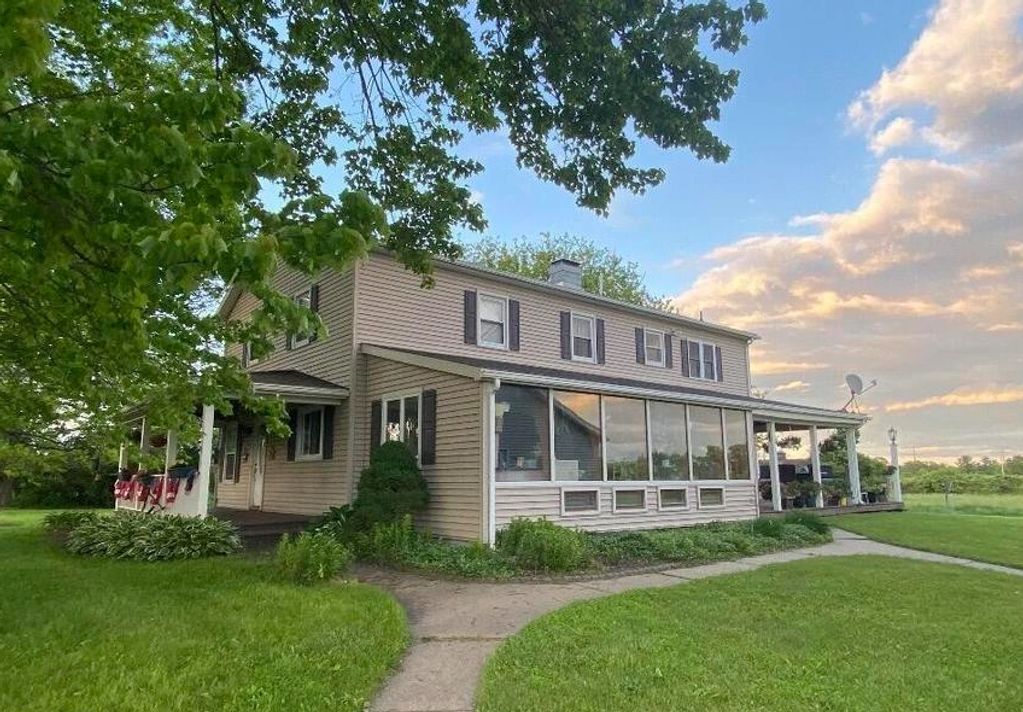 Two-story house with a porch surrounded by lush greenery under a partly cloudy sky.