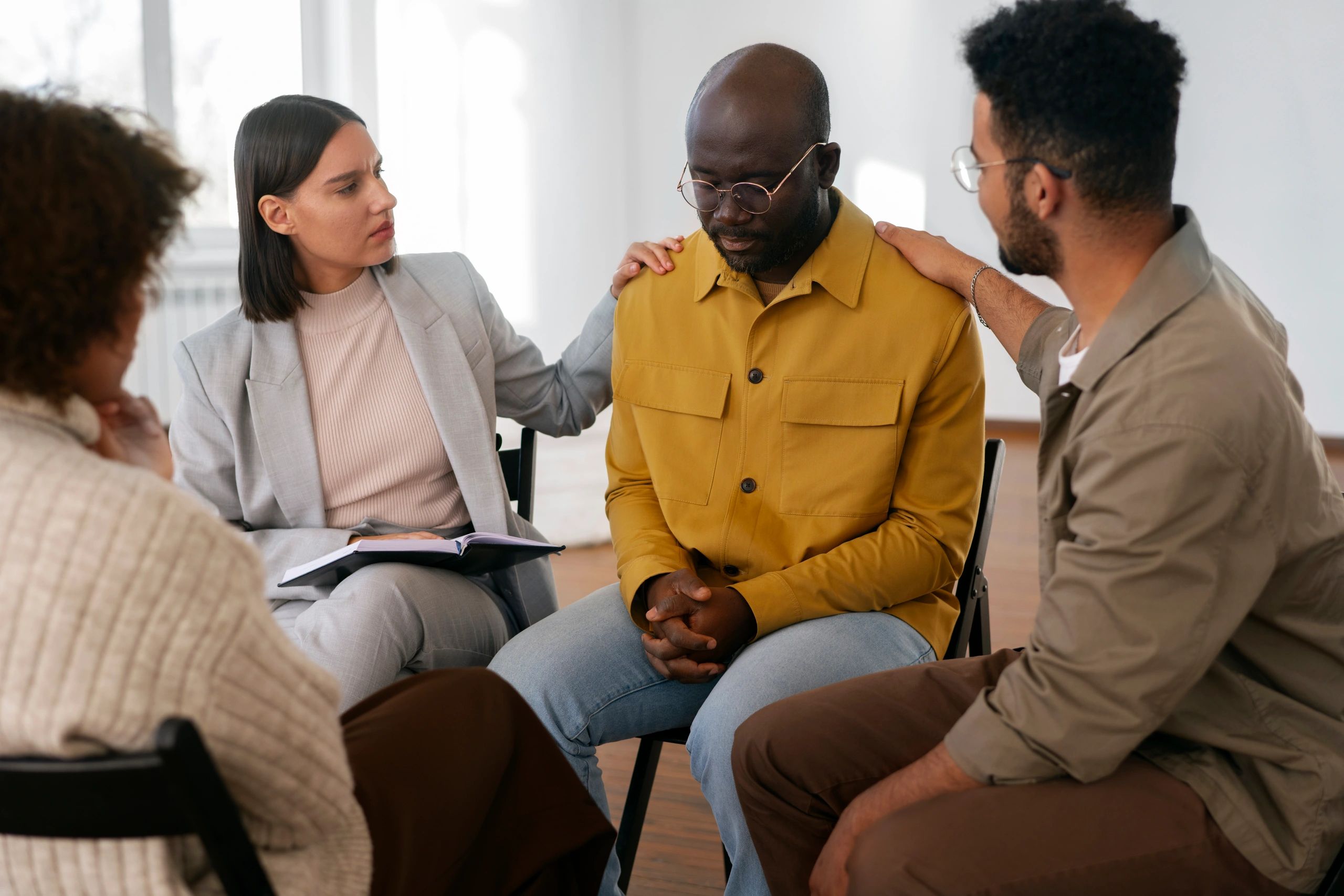 People comforting a man in emotional distress during a group therapy session.
