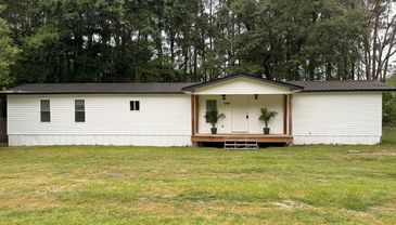 A white single-story modular home with a wooden porch and plants in front.