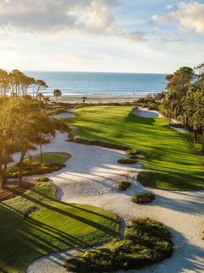 Sunlit golf course with ocean view and sand traps.