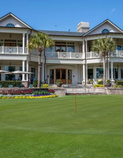 Elegant clubhouse overlooking a manicured golf green under a clear blue sky.