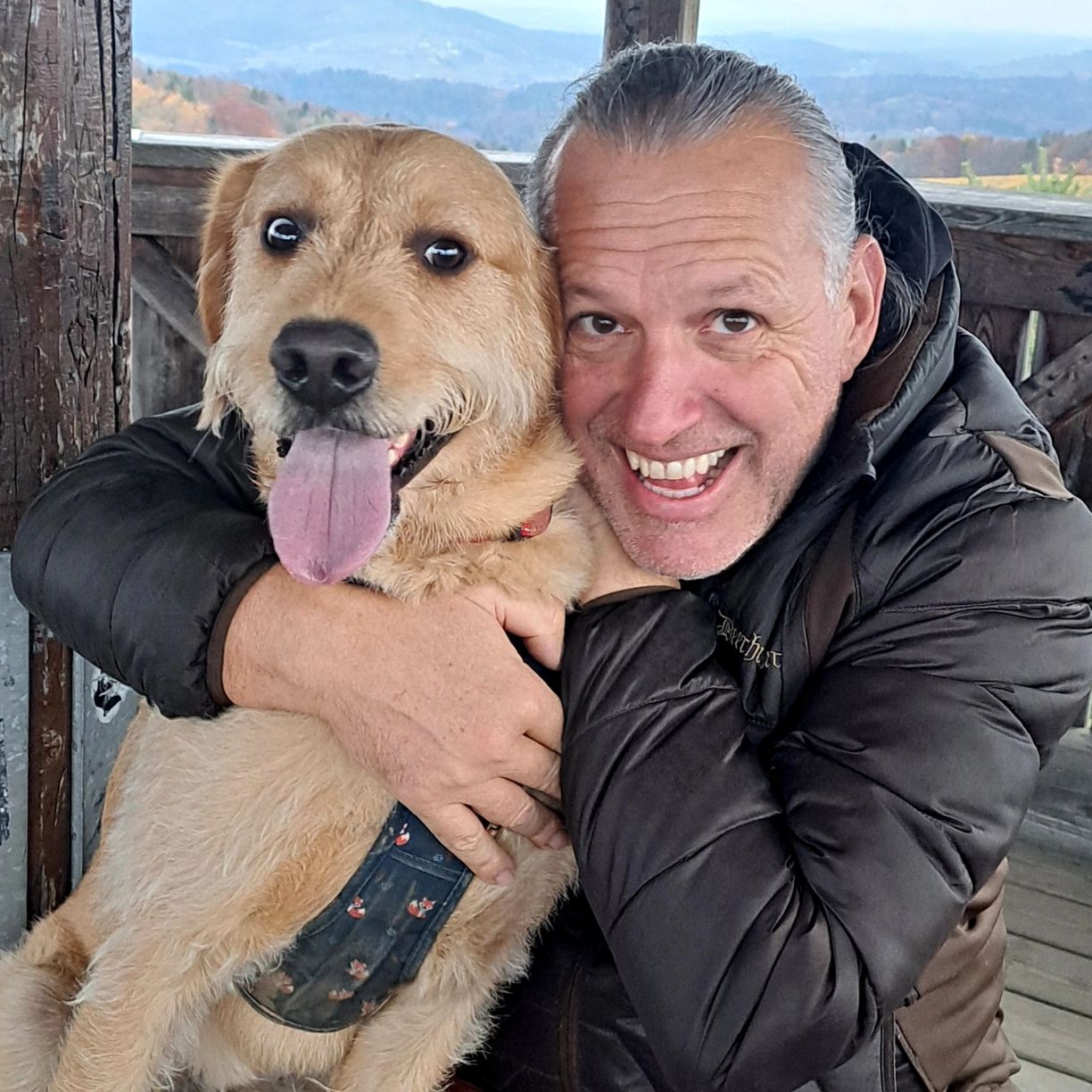 Mann umarmt glücklichen Hund mit heraushängender Zunge.