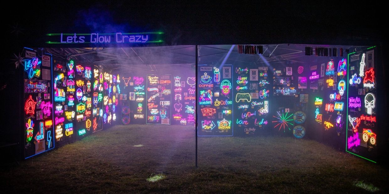 Vibrant neon signs glowing inside a tent with the sign 'Lets Glow Crazy' above.