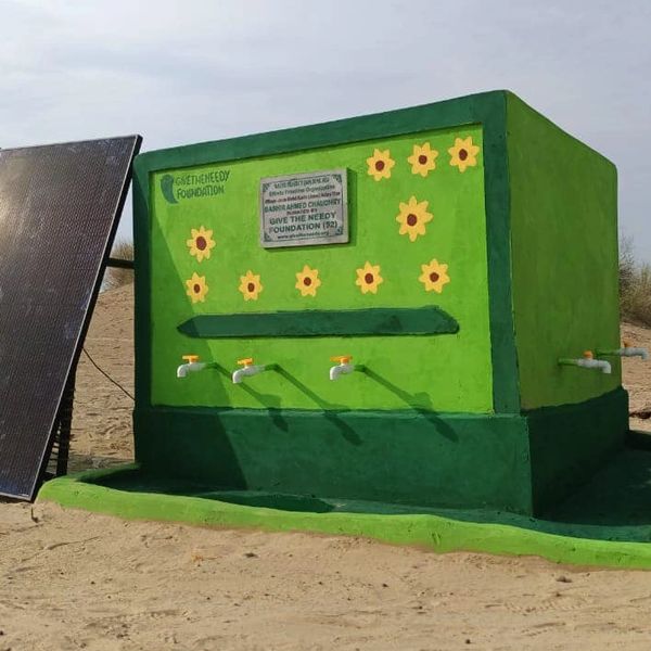 Green water station with taps and solar panel in sandy area.